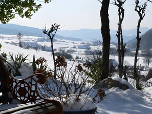 Eine Bank mit Blick auf eine verschneite Landschaft, mit kahlen Bäumen und weiter Ferne.