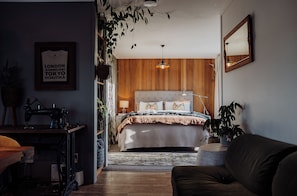 A bedroom with a wooden headboard, a bed with patterned bedding, a sewing machine, and a mirror on the wall.