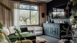 Ein Wohnzimmer mit einem grünen Sofa, einem Kamin, einem Fernseher und einem Fenster mit Blick auf Bäume.