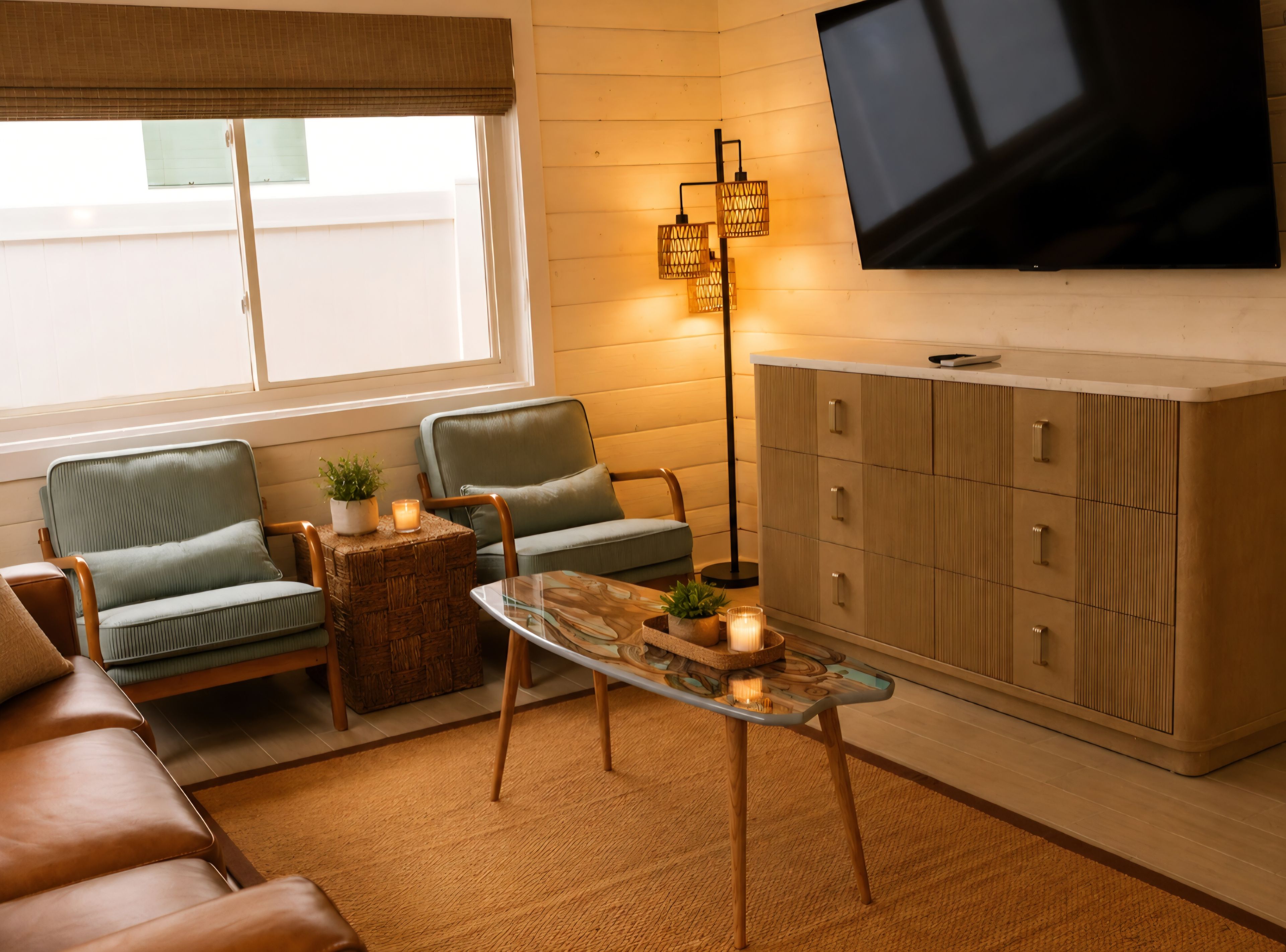 Un salon comprenant un canapé, deux fauteuils, une table basse en verre, un lampadaire, un téléviseur et un meuble.