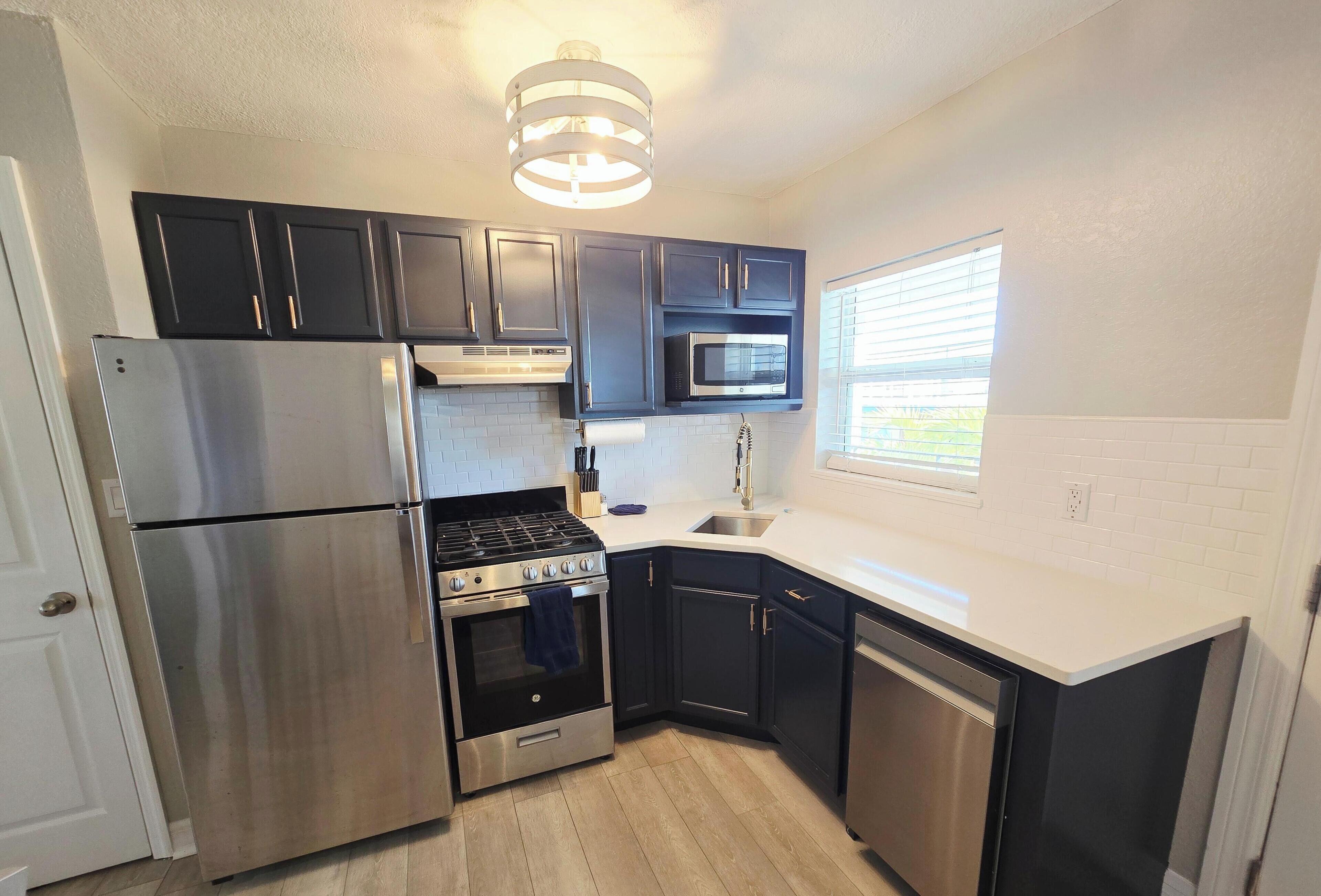 A compact kitchen with dark cabinets, stainless steel appliances, and a white countertop.