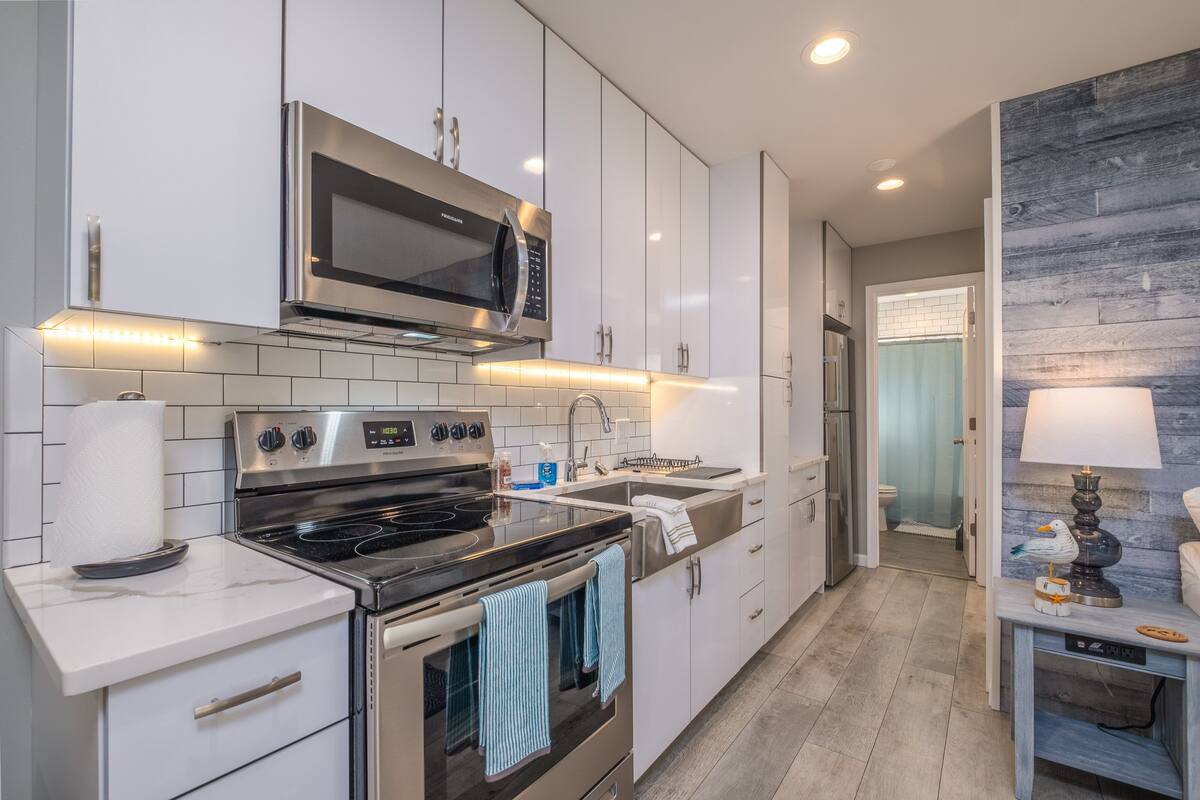 A modern kitchen with stainless steel appliances, white cabinetry, and a wooden accent wall.