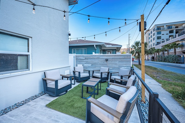 An outdoor seating area with multiple chairs and tables, a small lawn, and a building in the background. - Blue Wave Suites (Clearwater Beach)