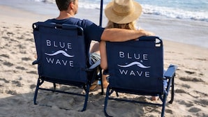 Two people sitting on beach chairs with 'Blue Wave' branding, facing the ocean. - Blue Wave Suites (Clearwater Beach)
