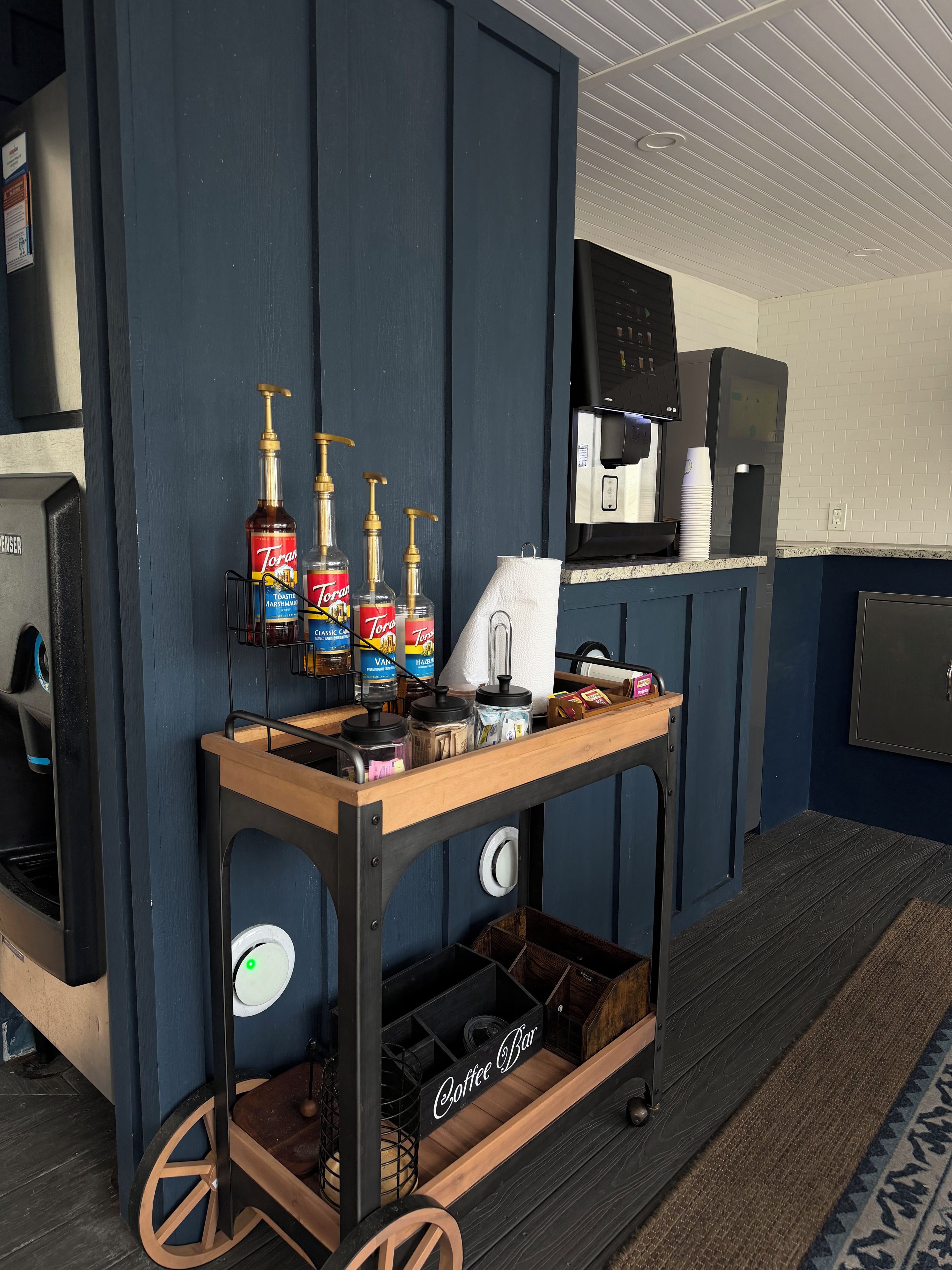 A coffee bar with Torani syrups, a coffee machine, and a paper towel dispenser.