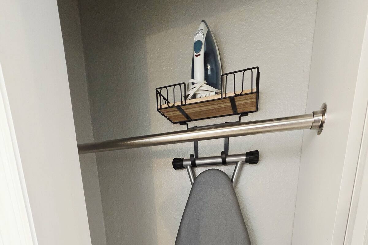 A bathroom with a towel rack holding a gray towel and an iron on a wall-mounted shelf.