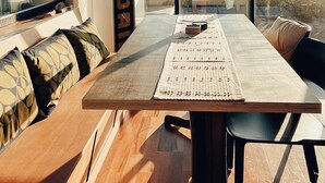A modern dining area with a wooden table, black chairs, and a large window offering a view of the outdoors. - Kowhai Cabin - Serene Scandi Escape in Hokitika (Hokitika)