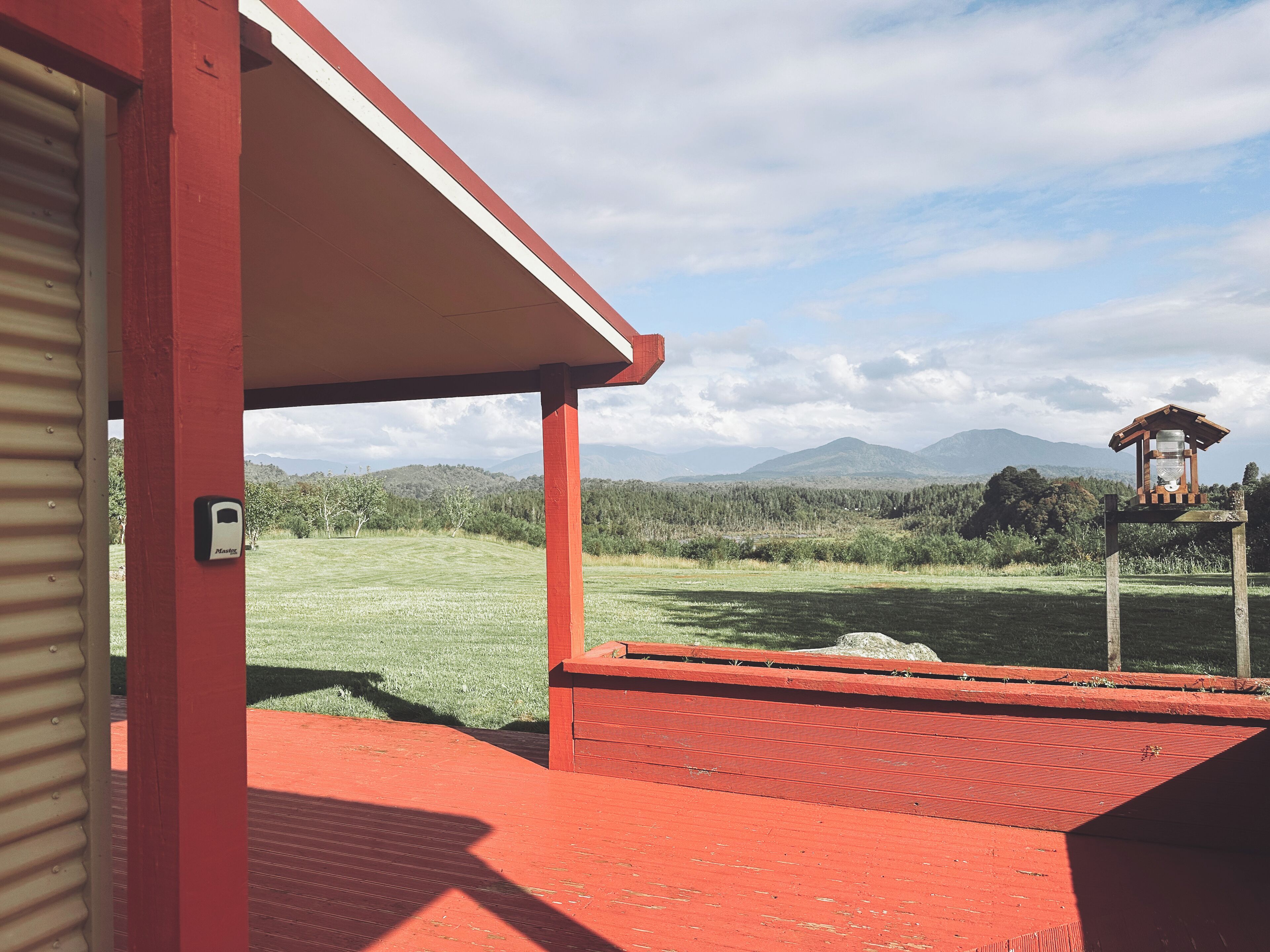 Un bâtiment rouge qui offre une vue sur un champ verdoyant et des montagnes au loin.