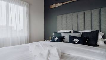 Ein ordentlich bezogenes Bett mit weißen Leinen und einem gefalteten Handtuch, ein Kopfteil mit geometrischem Muster und ein hölzernes Objekt an der Wand.