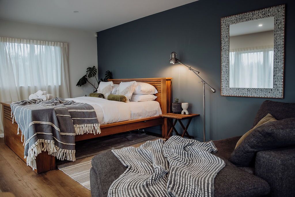 Ein modernes Schlafzimmer mit einem hölzernen Bett, einer Nachttischlampe, einem Spiegel und einem grauen Sofa.