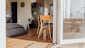 A modern living room with a sofa, wooden dining table, chairs, and a large window.
