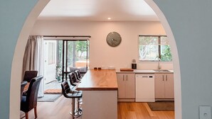 A modern kitchen with a central island, white cabinets, and a large window. - The Sundowner Beach Club (Hokitika)