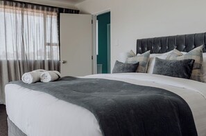 Una cama bien hecha con edredón gris y blanco, una manta gris y toallas blancas enrolladas a un lado.