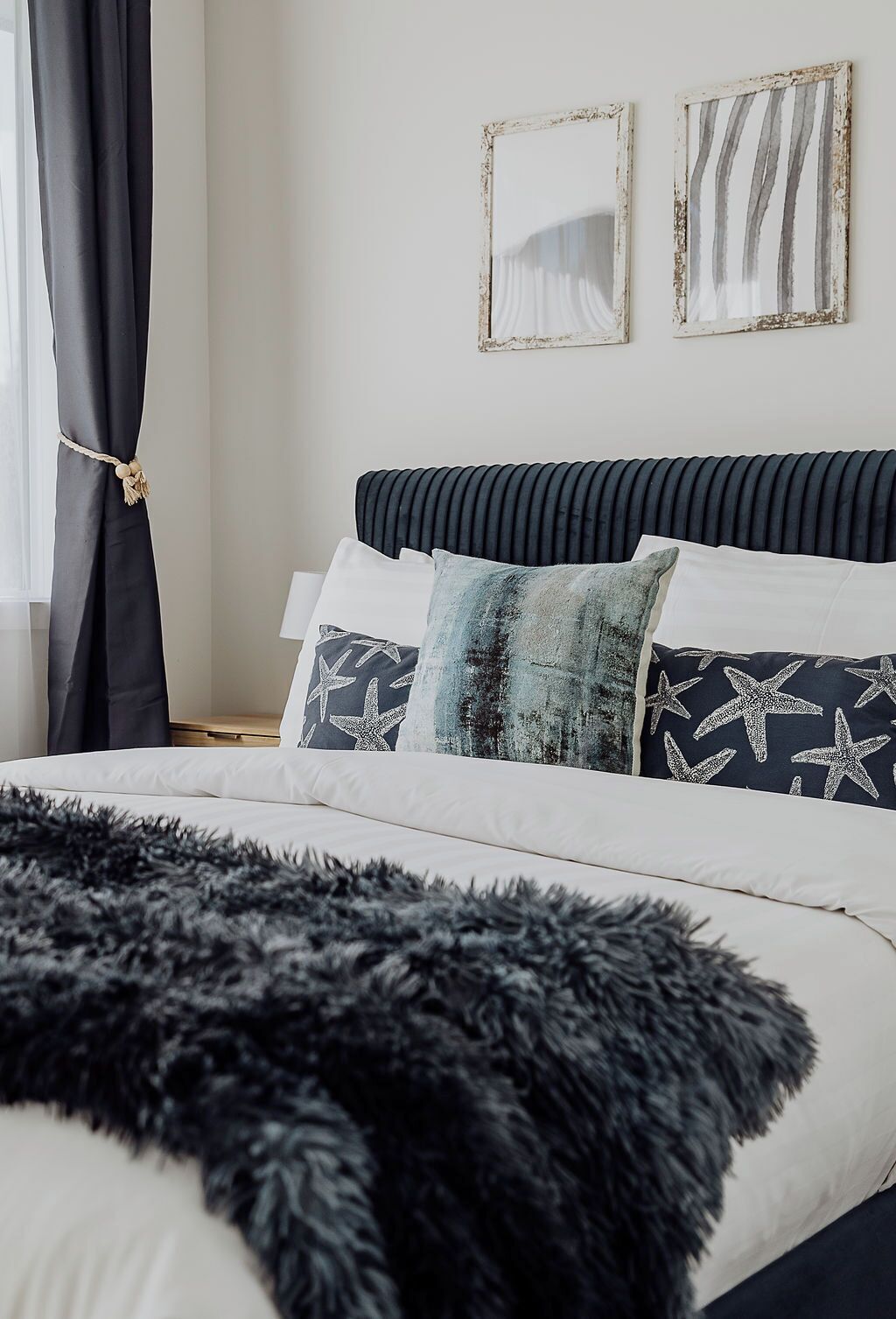 Un letto con una coperta nera in pelo, biancheria da letto bianca e cuscini decorati. Sopra il letto, due opere d'arte incorniciate.