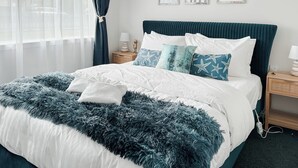 Una cama impecablemente tendida con una decoración en blanco y azul, una manta azul suave y una mesita de noche de madera con una lámpara.
