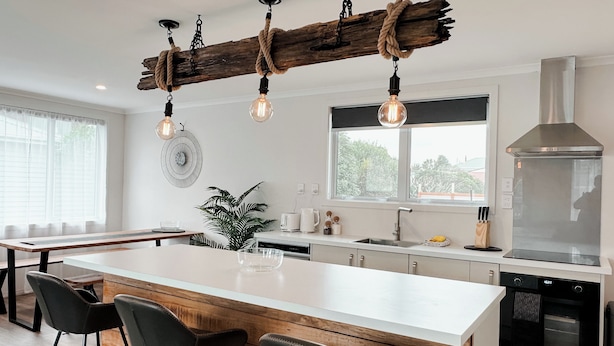Una cocina moderna con una isla grande, taburetes de bar, una lámpara colgante y un ventanal amplio.