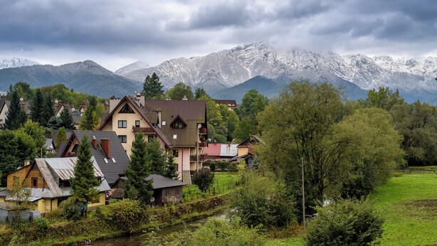 A rural village with houses, a river, and snow-capped mountains in the background.