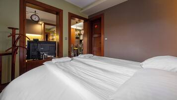 A hotel room with a large bed, a television, and a clock on the wall.