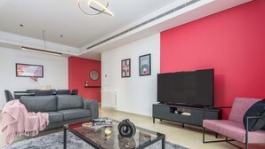 A modern living room with a grey sofa, a black coffee table, and a red accent wall. - Viva 3-BR Apt in Waterfront Dbayeh (Dbayeh)