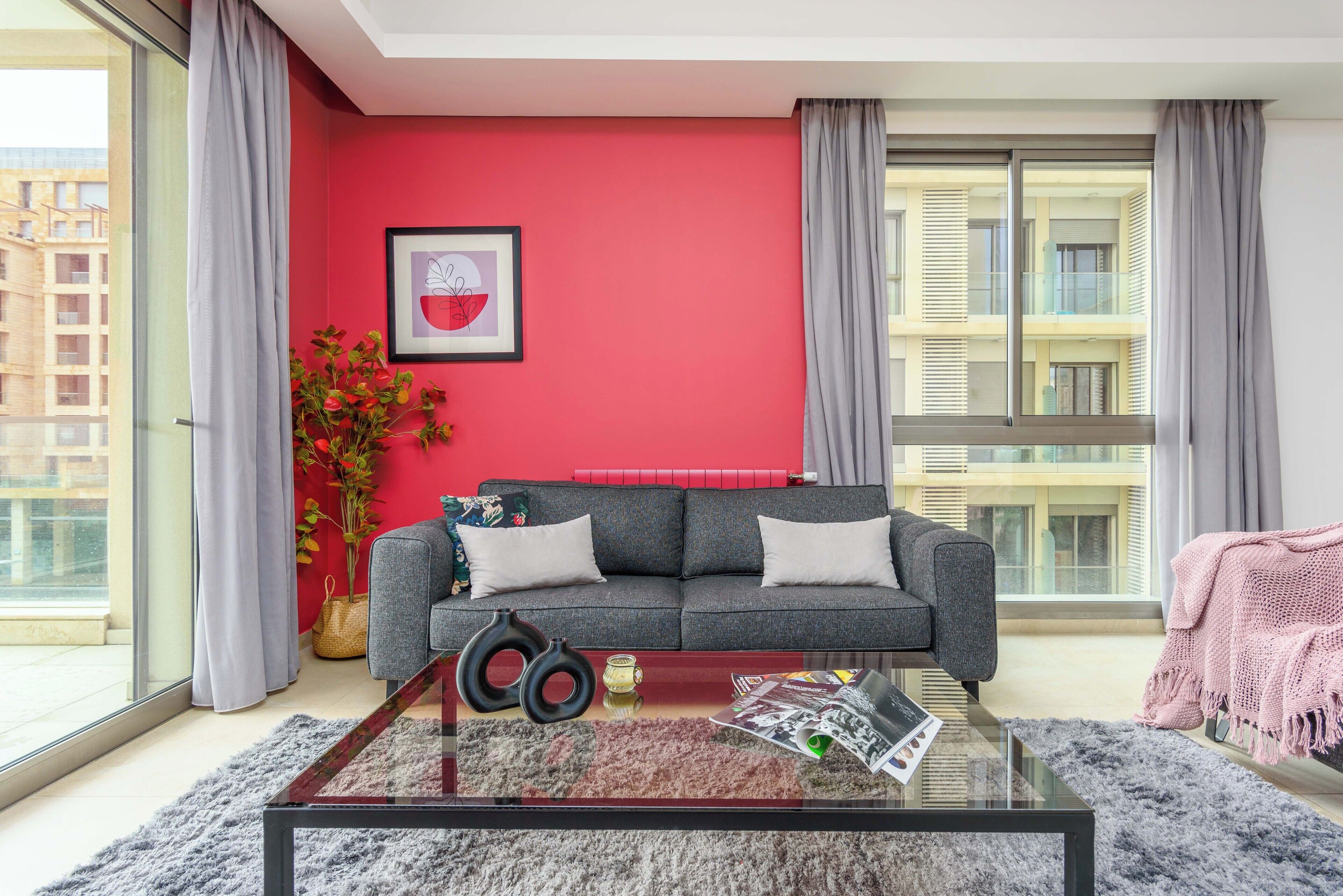 A modern living room with a grey sofa, a glass coffee table, and a red accent wall.