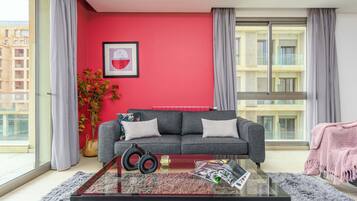 A modern living room with a grey sofa, a glass coffee table, and a red accent wall.