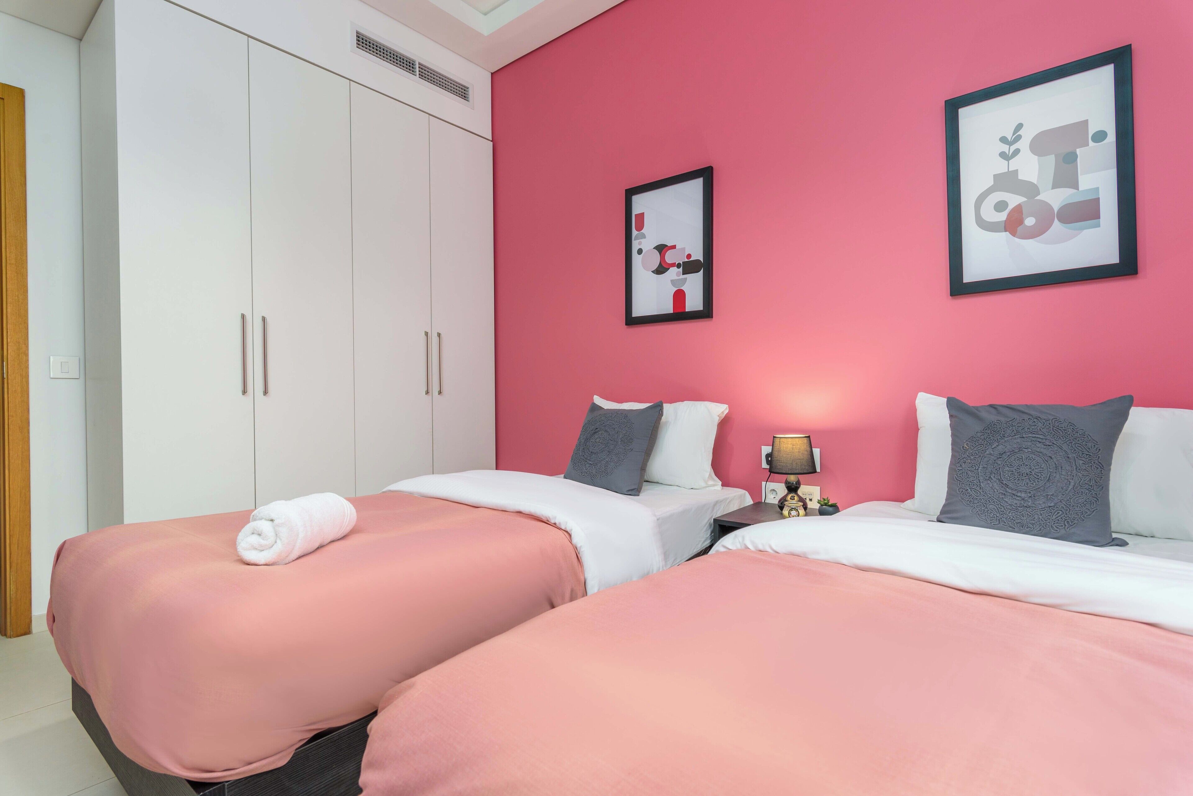 A room with two beds, a wardrobe, and two framed pictures on the wall.