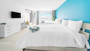 Quarto moderno com uma cama grande, televisão de tela plana, escrivaninha e vista para a cidade.