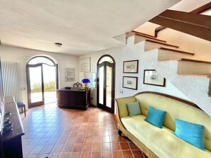A spacious living area with a sofa, a desk, and a lamp. There are framed pictures on the wall and a window with a view.