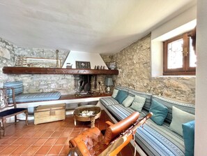 Ein gemütliches Wohnzimmer mit einer Steinwand, einer hölzernen Bank, einer Couch mit gemusterten Kissen und einem Ledersessel.