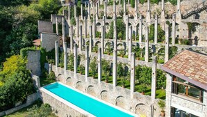 Une construction en pierre dotée d’une piscine, entourée de verdure et de bâtiments modernes.