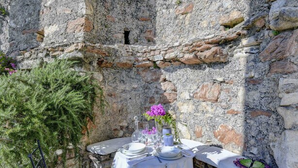 Une table dressée pour deux personnes, avec une nappe blanche, une carafe en verre et des fleurs violettes.