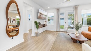 Een ruime woonkamer met een grote spiegel, een flatscreen-televisie, een plafondventilator en een groot raam met gordijnen.