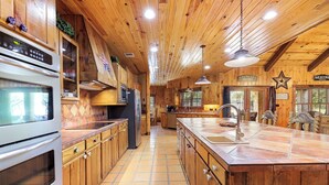 Eine geräumige Küche mit Holzausstattung, einer großen Kochinsel und einem modernen, edlen Kühlschrank aus Edelstahl.