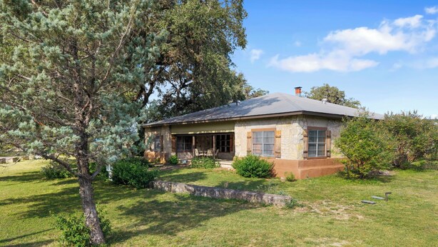 A stone house with a porch, surrounded by grass and trees. - Big Oak@ FrioRiverVacationRentals (Concan)
