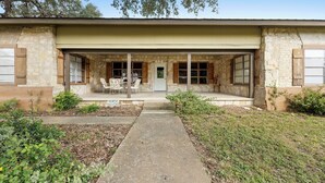 A stone building with a covered porch, a concrete pathway, and a small garden area. - Big Oak@ FrioRiverVacationRentals (Concan)