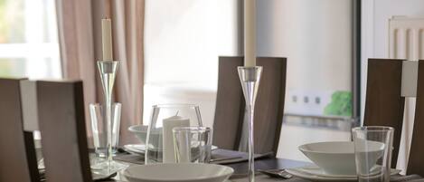 A dining table set with white plates, clear glasses, and a tall candle in a glass holder.