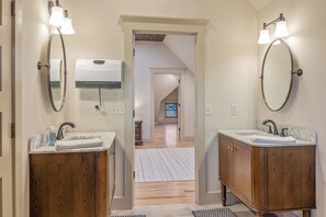 Une salle de bain avec deux lavabos, des meubles en bois et un miroir. On y trouve un sèche-mains et un porte-serviettes au-dessus des lavabos.