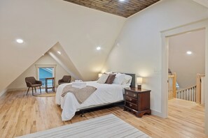 Une chambre avec un plafond en pente, un lit recouvert de draps blancs, une commode en bois et une chaise.