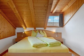 A wooden ceiling, a bed with pillows, a nightstand, and a window with a curtain.