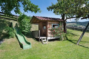 A wooden cabin with a small porch, a green slide, and a flower box.