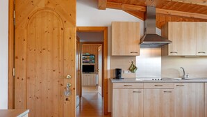 A wooden door, a kitchen with cabinets and a stove, and a hallway leading to a living area.