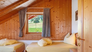 A wooden cabin with two beds, a window with curtains, and a door.