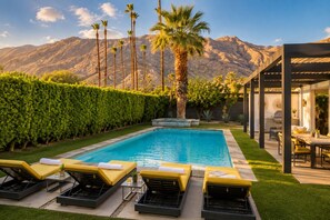 A swimming pool with lounge chairs, a barbecue area, and a view of mountains.