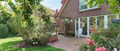 A garden with a brick house, a wooden pergola, and a white chair.