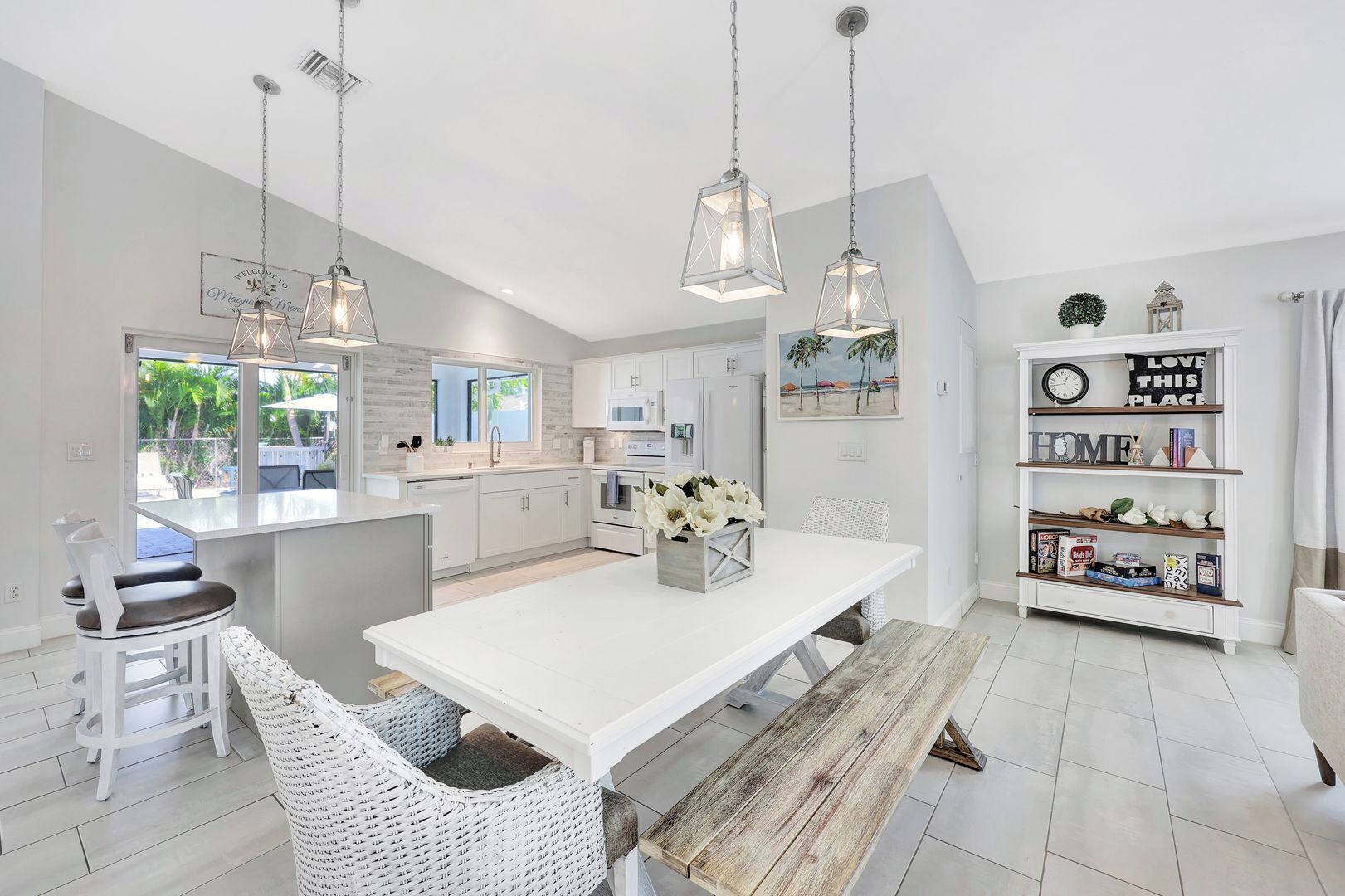 A modern kitchen with white cabinetry, a central island, pendant lights, and a view of the outdoors.