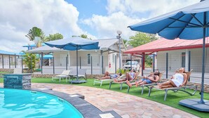 A poolside area with lounge chairs and umbrellas, a stone-tiled deck, and a clear blue pool.