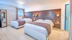 A hotel room with two beds, a large mirror, a wooden headboard, and a view of the sea through a window.
