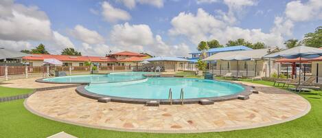 A pool area with two pools, lounge chairs, and a covered seating area.