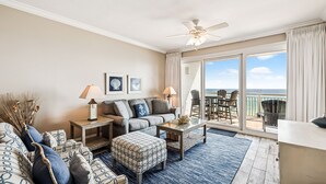 A spacious living room with a large window offering a view of the ocean, a ceiling fan, and a balcony with outdoor seating. - HP 35W Gulf Front Condo @ High Pointe | Lagoon Pool | Tennis & Pickleball Courts (High Pointe Resort)