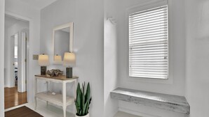 Een schone, witte kamer met een bankje, een spiegel, twee lampen en een potplant.